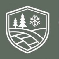 A white shield emblem on a green background featuring two pine trees, a snowflake, and stylized fields or rolling hills.