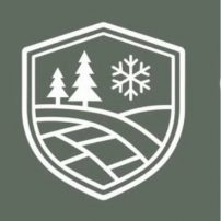 A white shield emblem on a green background featuring two pine trees, a snowflake, and curved lines representing a landscape or road.